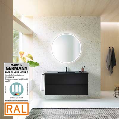 Modernes Badezimmer mit burgbad-Badmöbel, rundem Spiegel, „Made in Germany“- und RAL-Zertifikat links im Bild. 